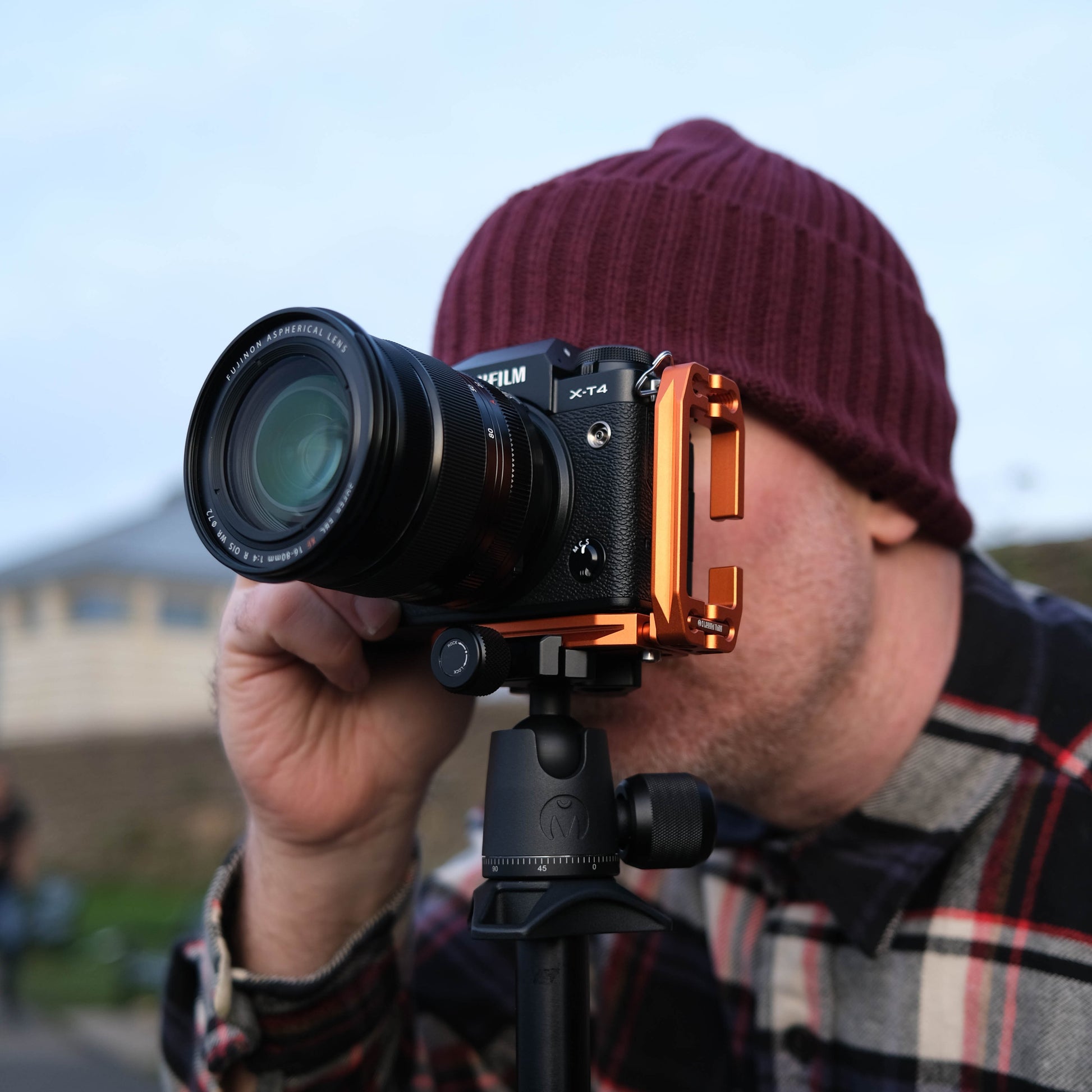 Person holding a camera with a lens attachment, wearing a beanie and plaid shirt.