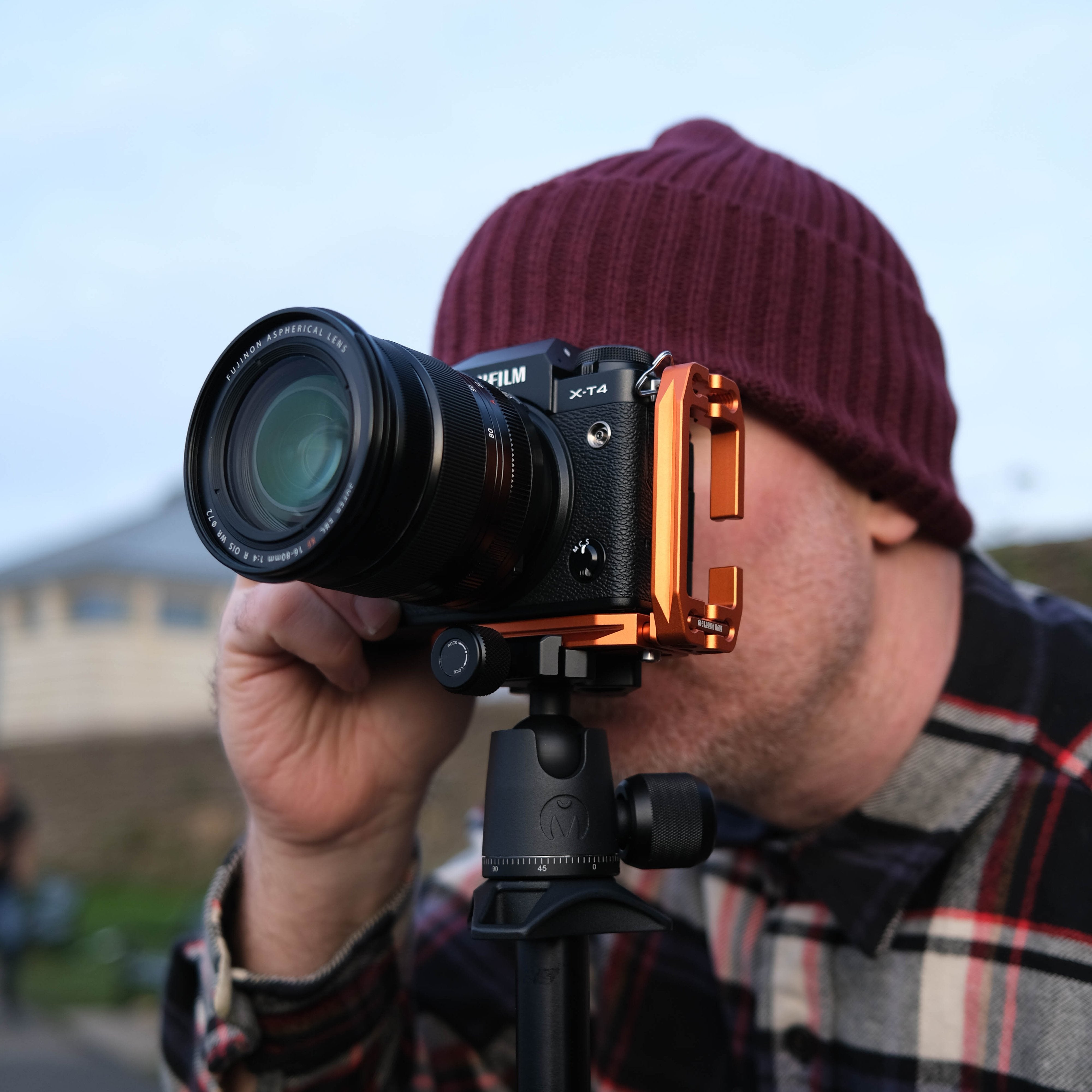 Person holding a camera with a lens attachment, wearing a beanie and plaid shirt.