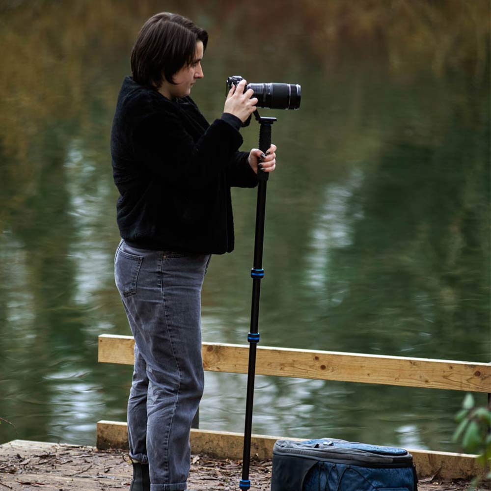 Person holding a camera with a monopod near a body of water