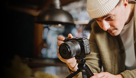 Man holding a camera on a tripod in a blurred indoor setting