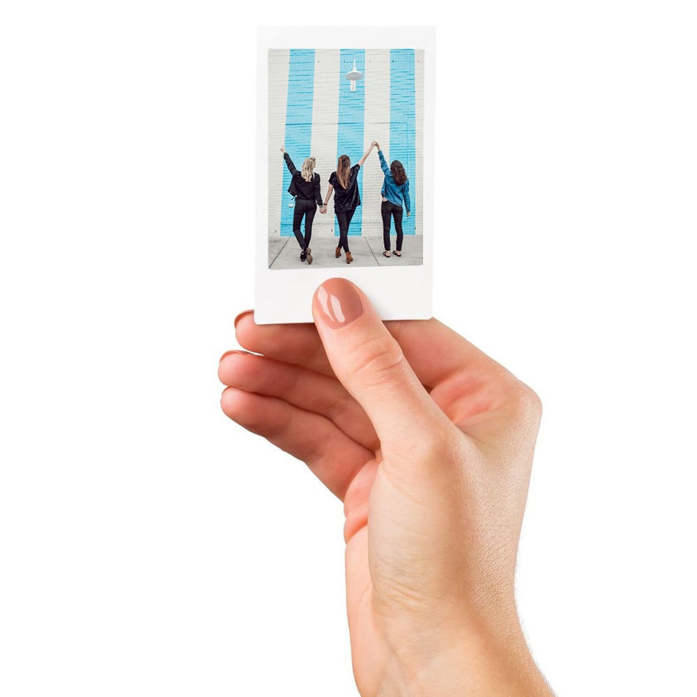 Hand holding a small photo print of three people in front of a blue door.