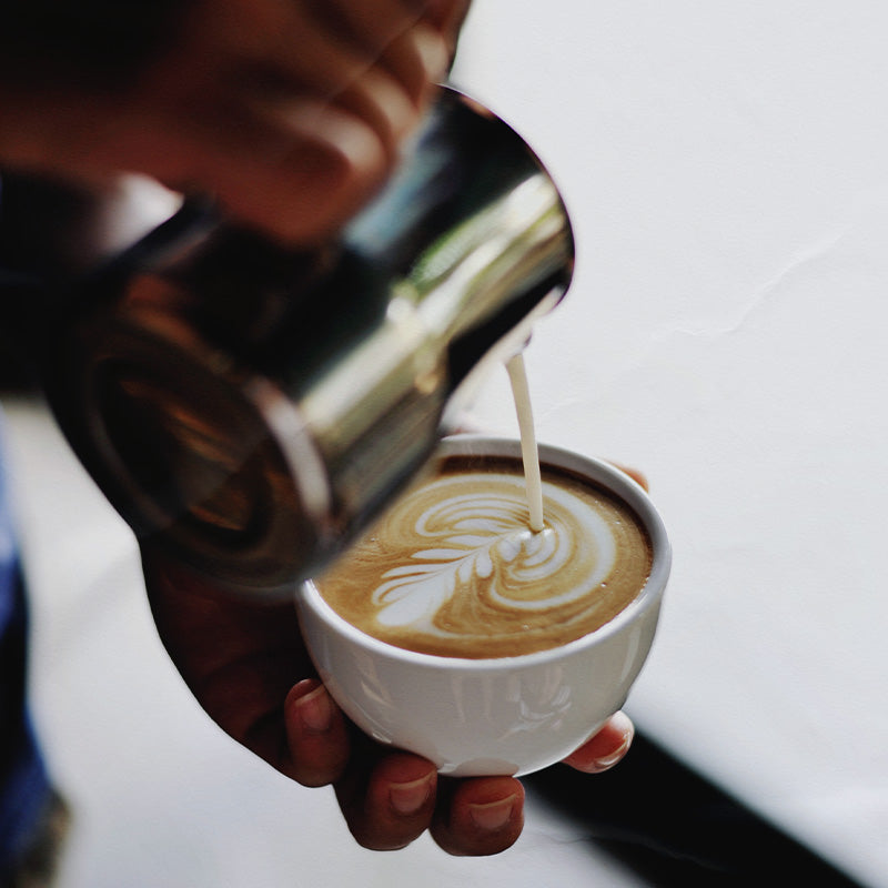 Person pouring milk into a cup of coffee with latte art.