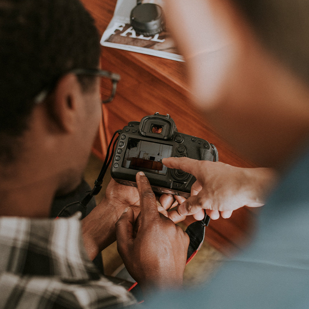 Two people holding a camera with a wooden surface in the background