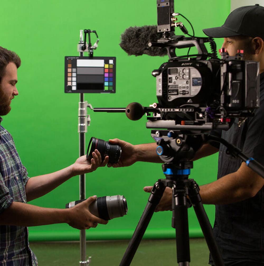 Two people working with camera equipment in front of a green screen