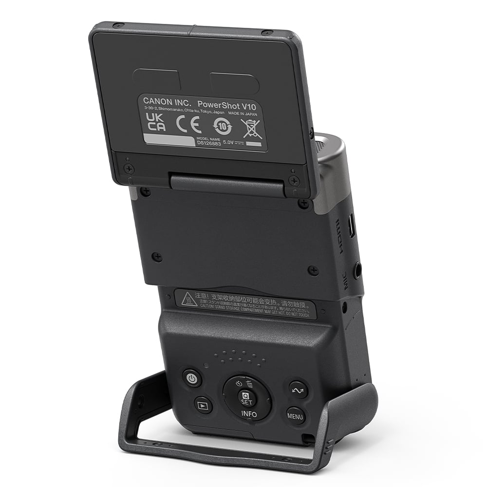 Canon PowerShot V10 vlog camera kit in silver — compact rectangular camera with wide-angle lens, flip-up screen, and integrated mini tripod stand.