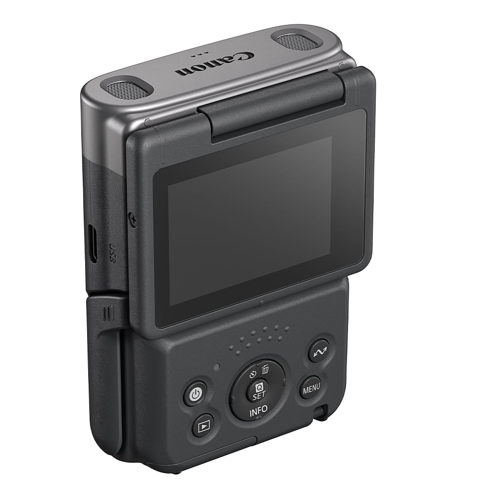 Canon PowerShot V10 vlog camera kit in silver — compact rectangular camera with wide-angle lens, flip-up screen, and integrated mini tripod stand.