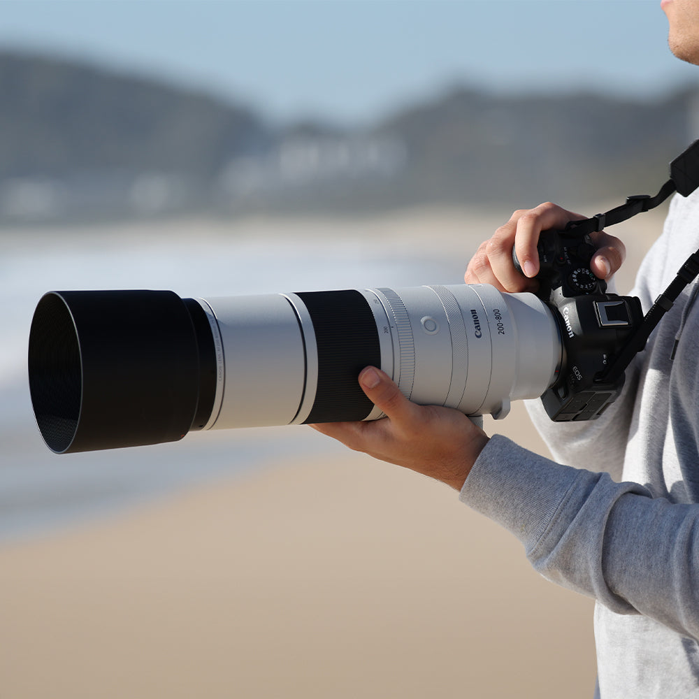 Person holding a camera with a large lens on a beach