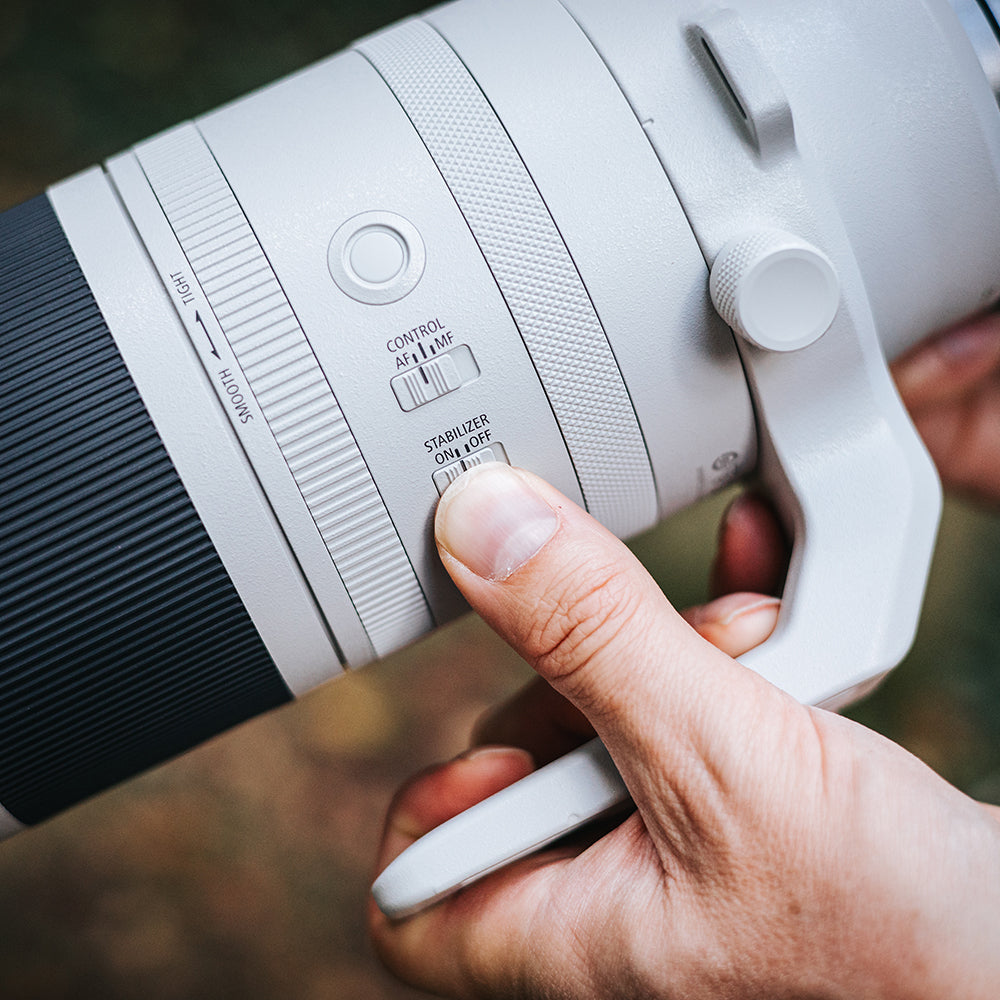 Close-up of a person holding a camera lens with a blurred natural background