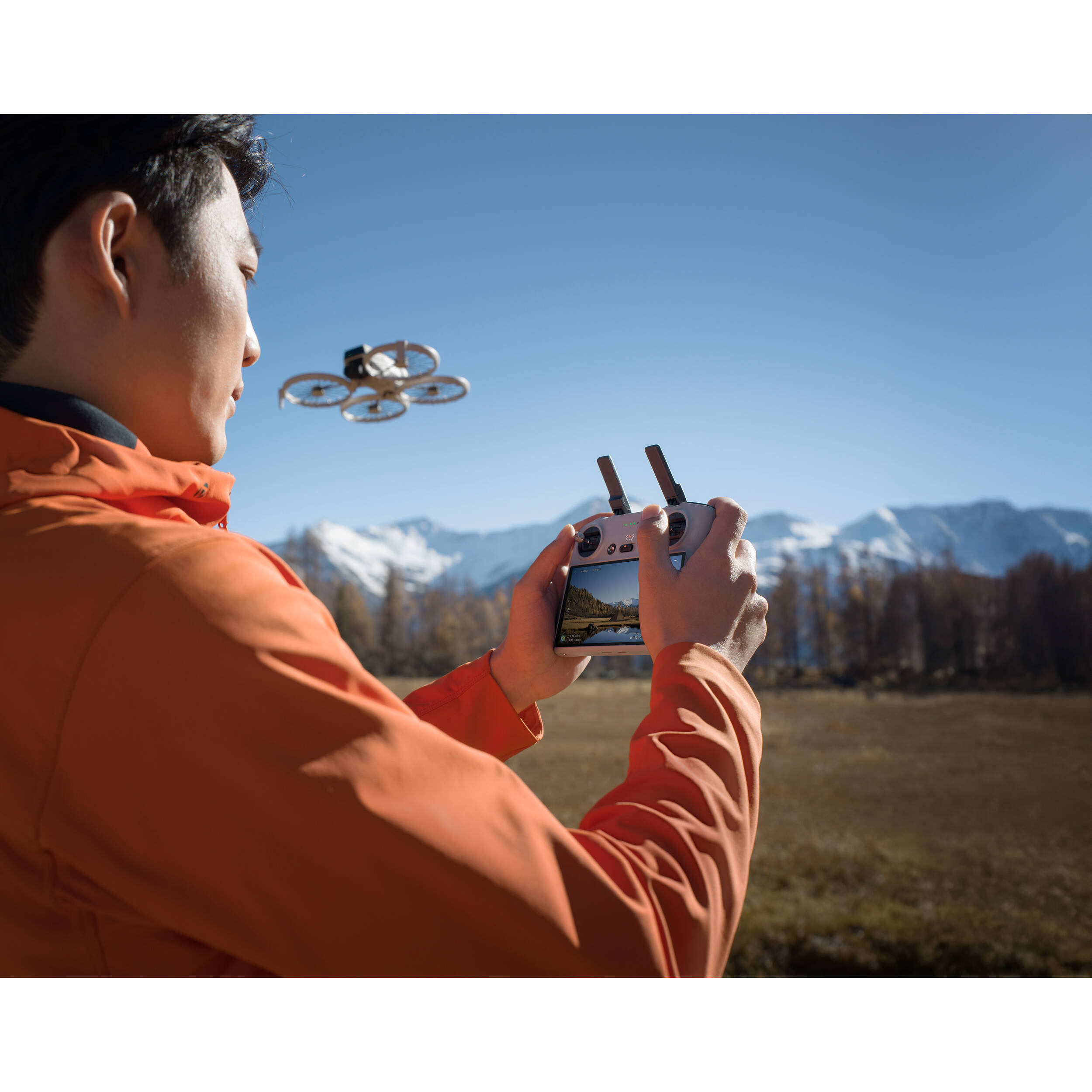 Person flying a drone in an open field with mountains in the background
