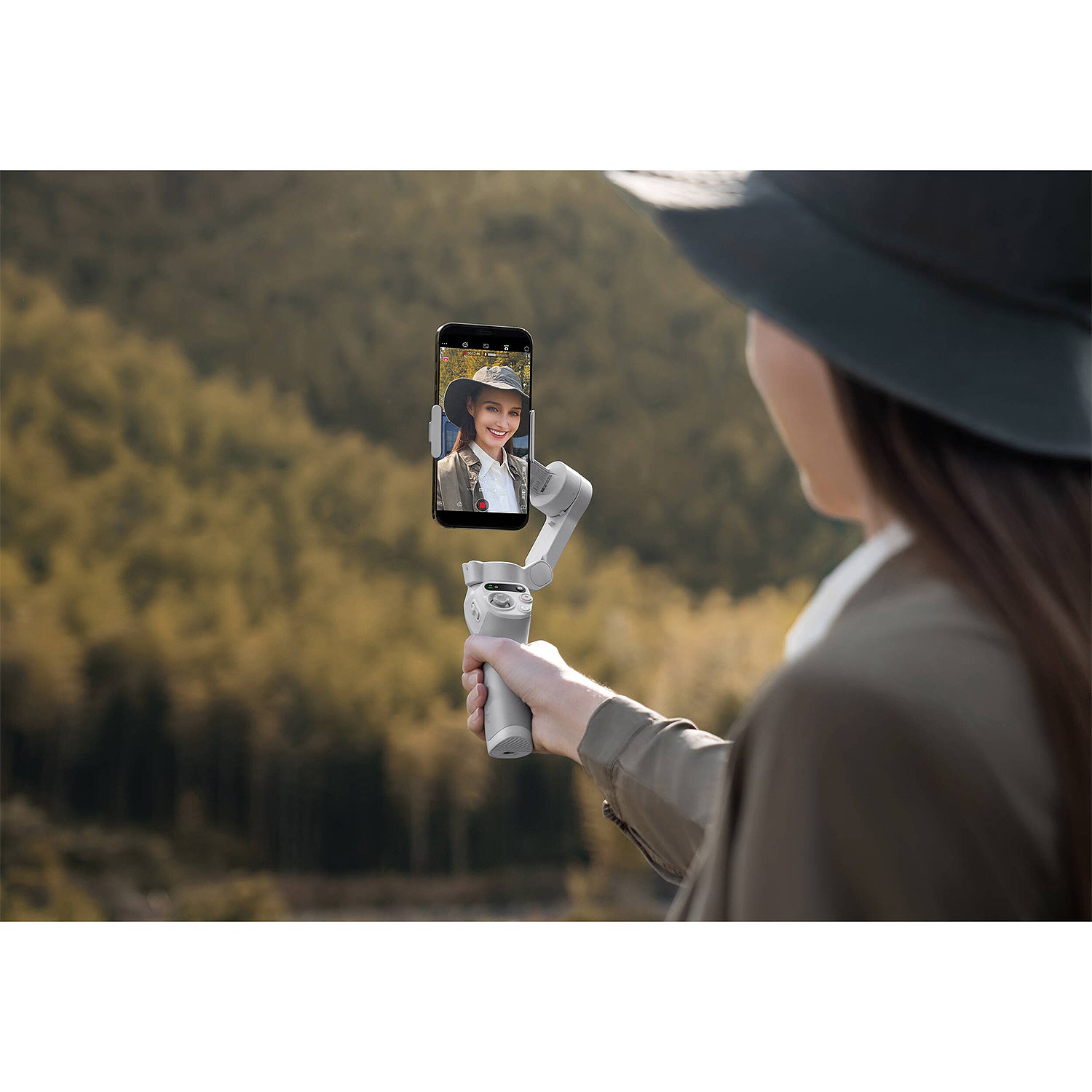 Person holding a smartphone with a gimbal in a natural setting