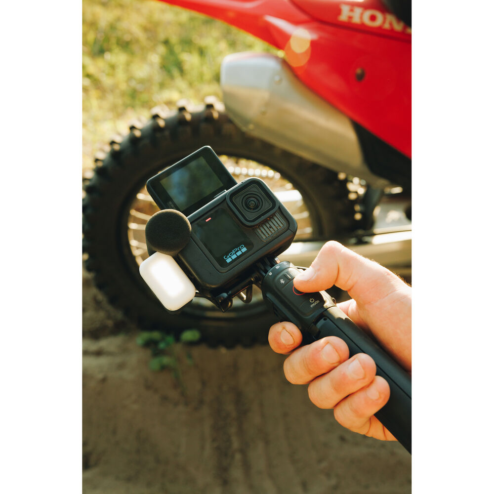 Action camera held by a hand with a dirt bike in the background