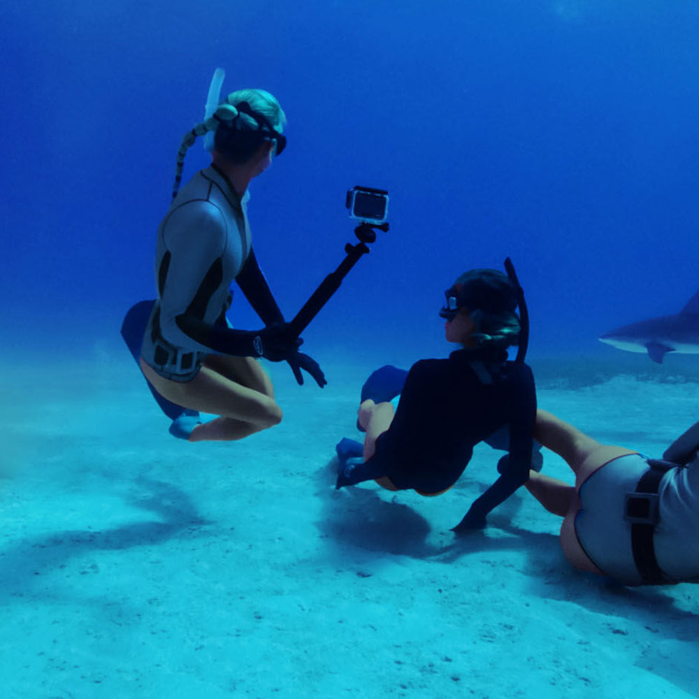 Two scuba divers underwater with a third person holding a camera.
