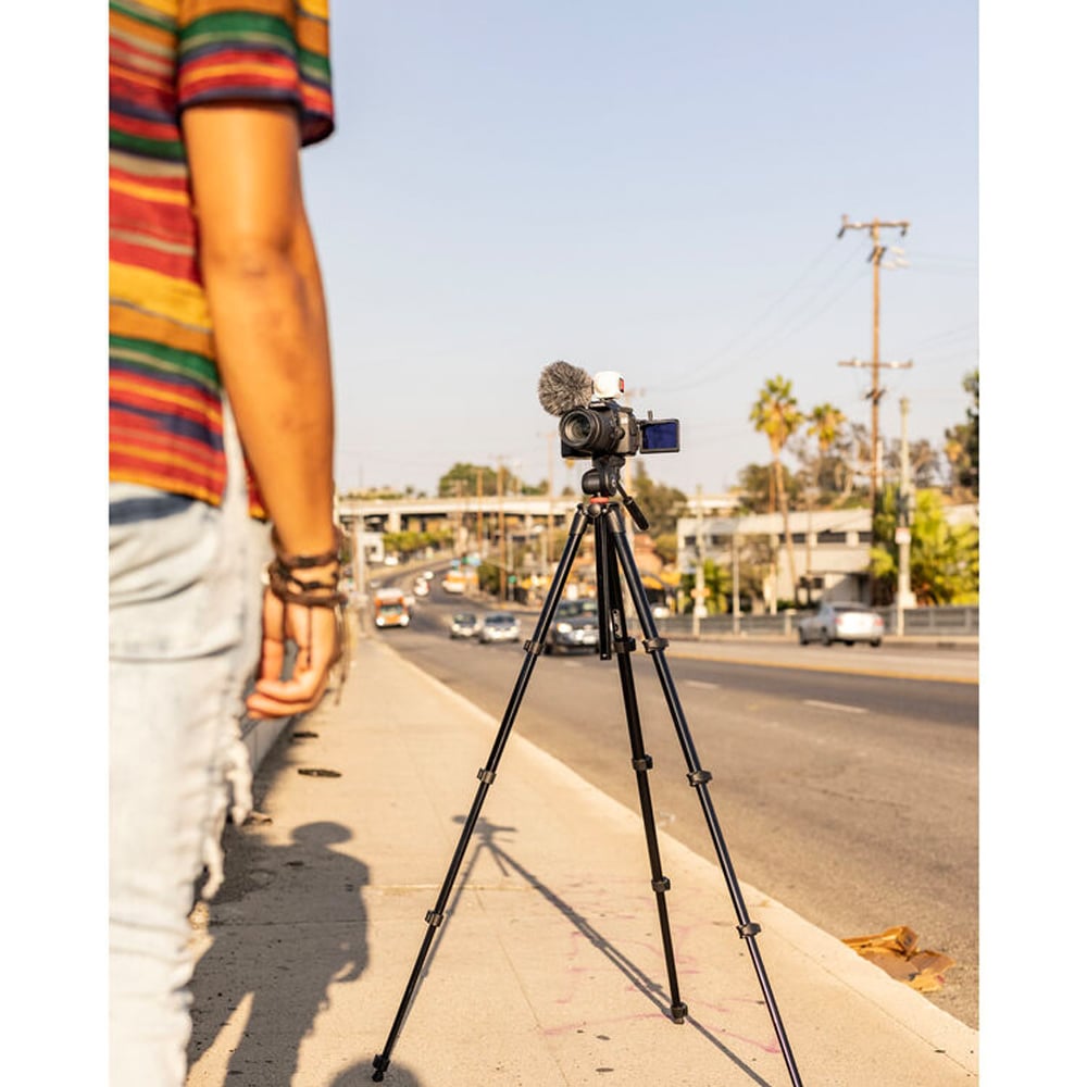 Person filming on a tripod with a camera and microphone on a city street.