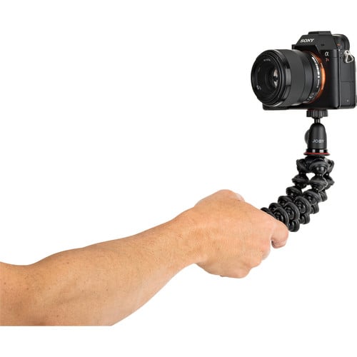 Camera mounted on a flexible tripod held by a person's hand against a white background