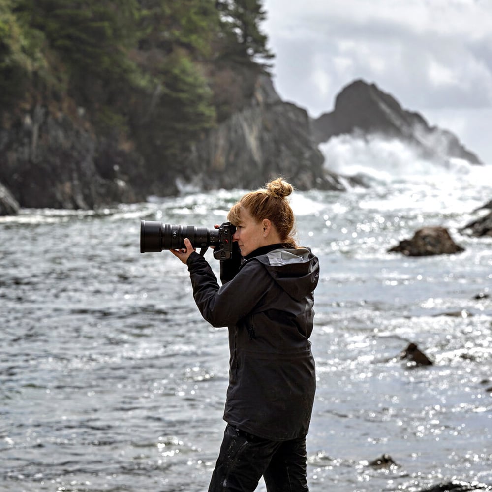 Woman standing by a body of water holding a Nikon camera with a Nikon 400mm lens.