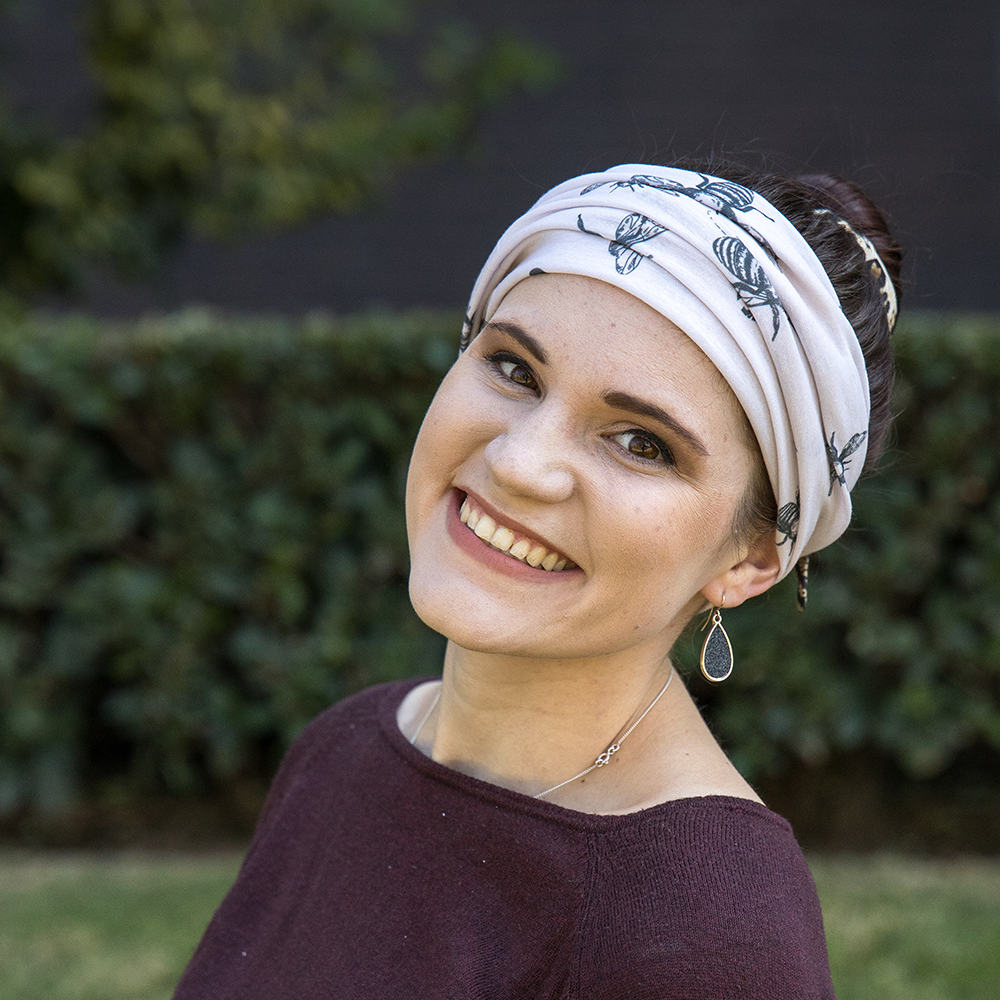 Woman wearing a headscarf with a floral pattern, smiling outdoors.