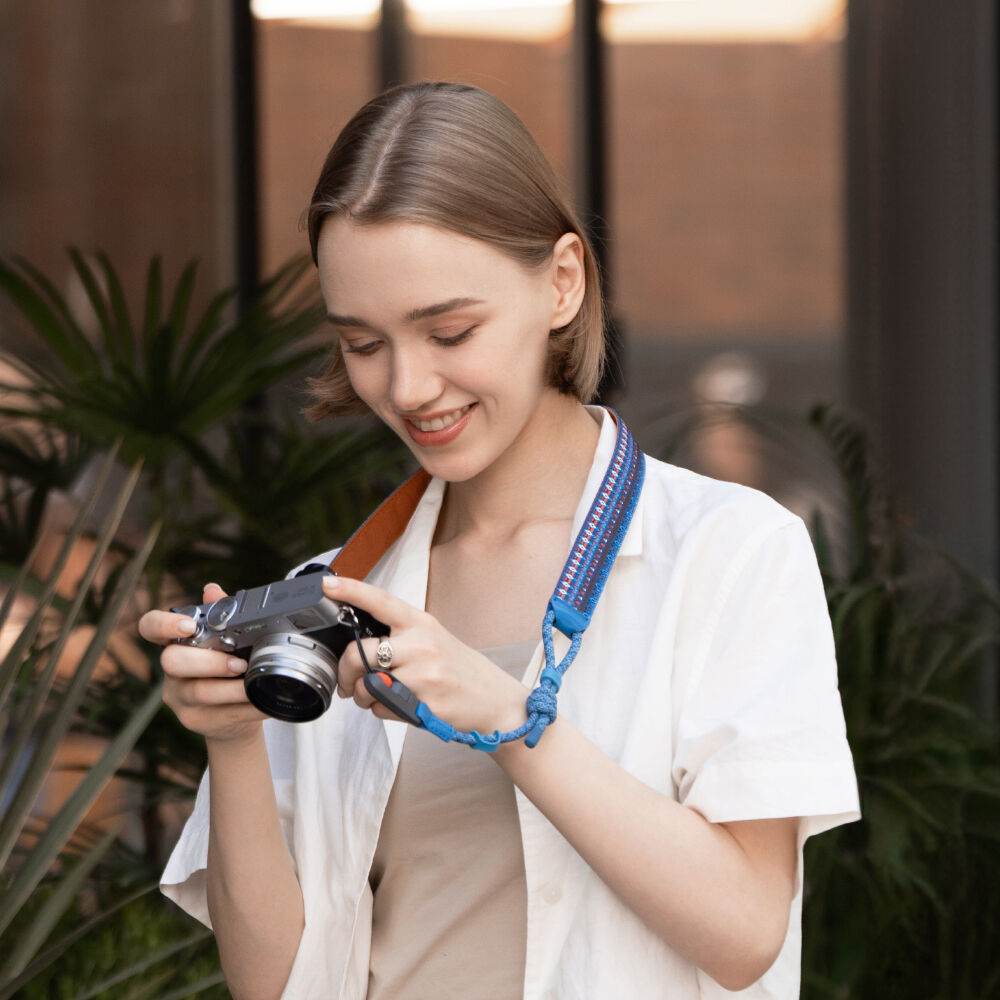 Woman holding a camera with a blue strap, surrounded by plants