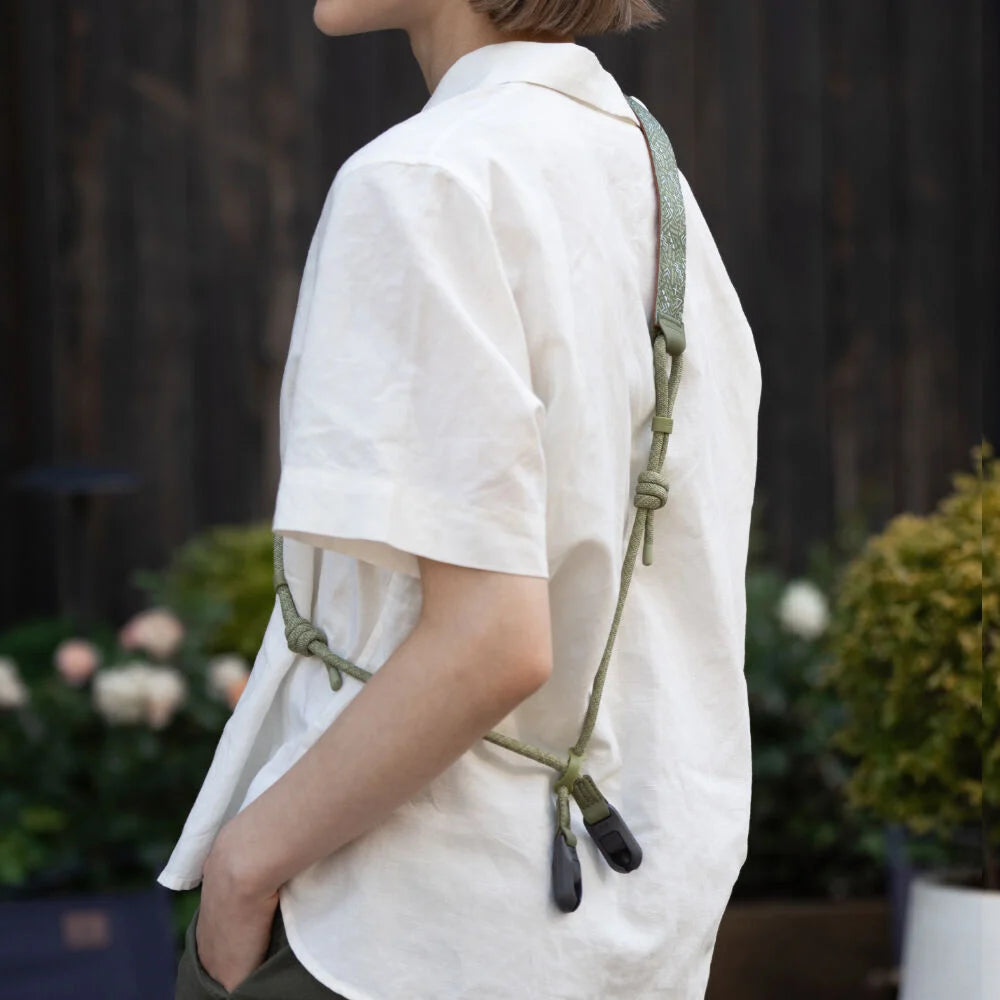 Person wearing a white shirt with a green knotted camera strap over their shoulder, standing outdoors.