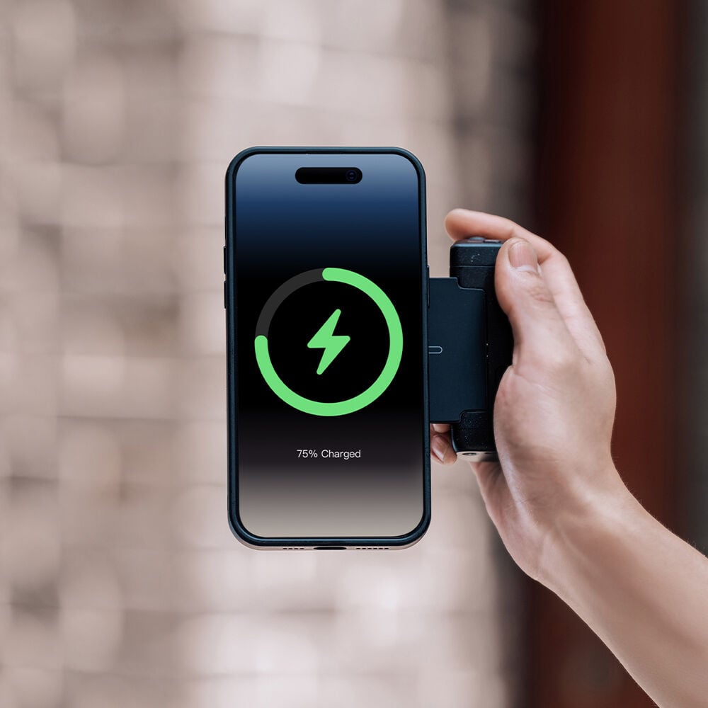Hand holding a smartphone with a charging app displaying 75% charge, against a blurred background.