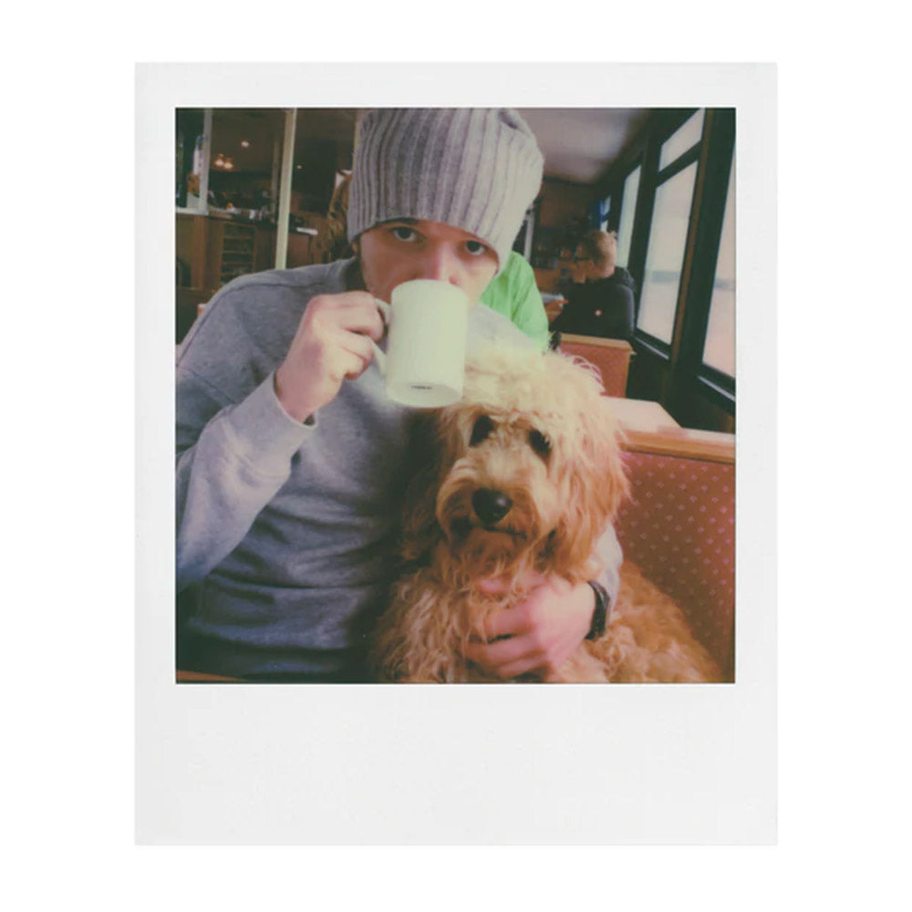 Person holding a mug with a dog sitting next to them, inside a vehicle.