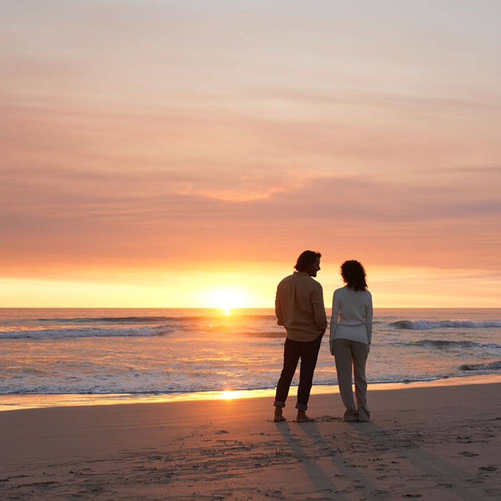 Two people standing on a beach at sunset