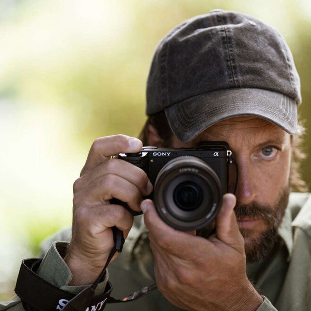 Man holding a Sony camera with a blurred natural background