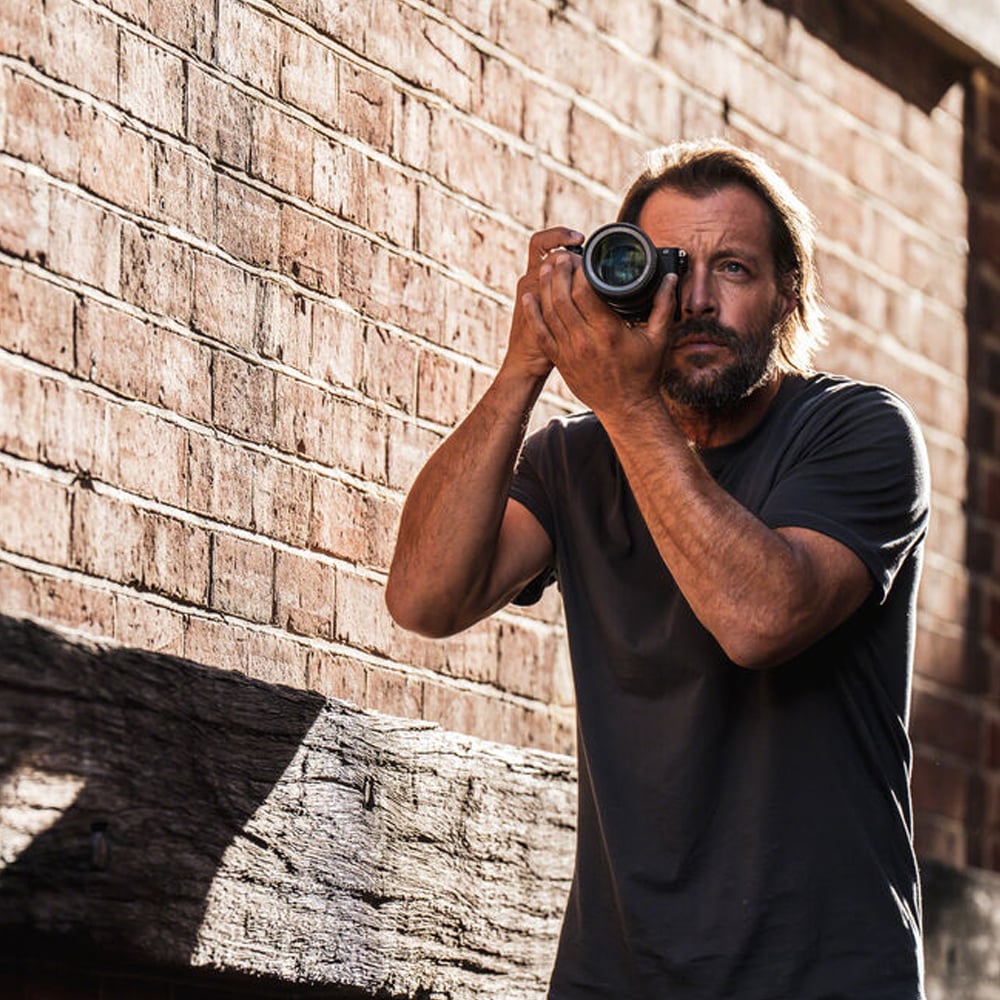 Man holding a camera against a brick wall