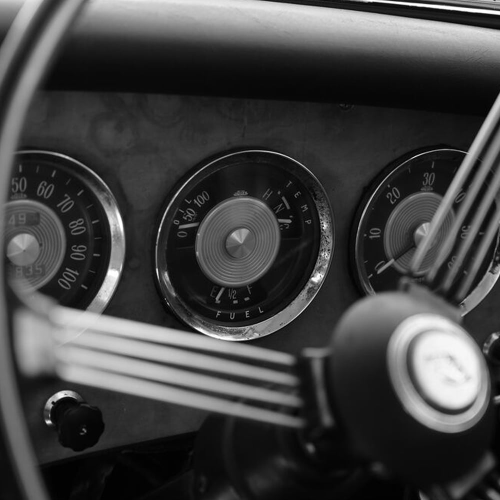 Close-up of a vintage car dashboard with gauges and steering wheel.