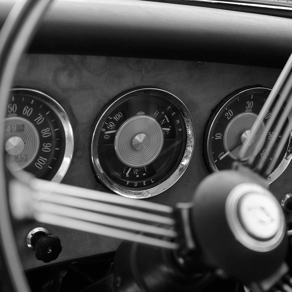 Close-up of a vintage car dashboard with gauges and steering wheel.