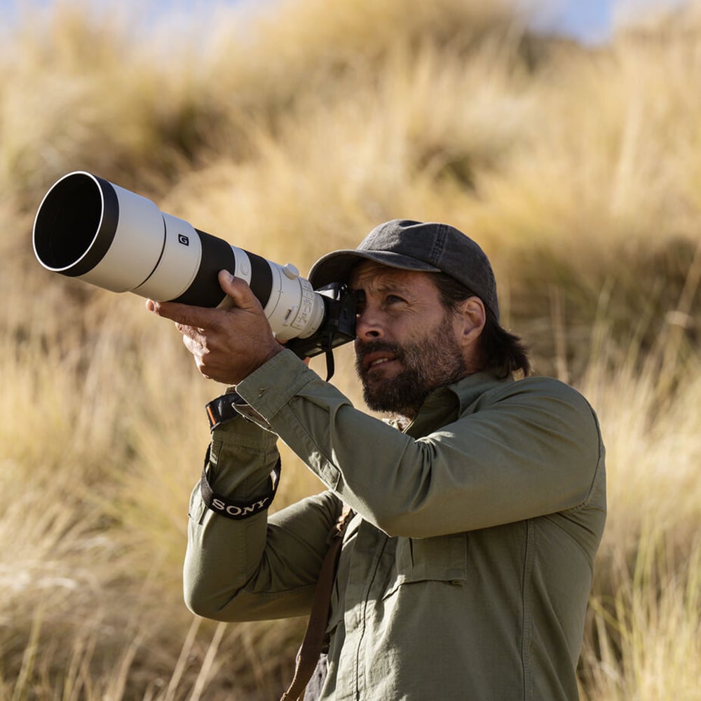 Man holding a camera with a large lens in a natural setting