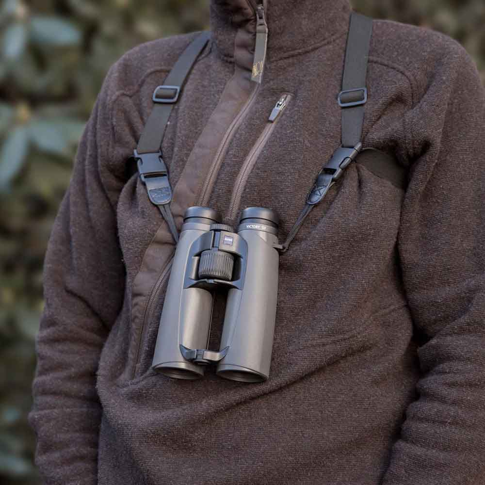 Person wearing a brown jacket with binoculars attached to a strap over their chest.